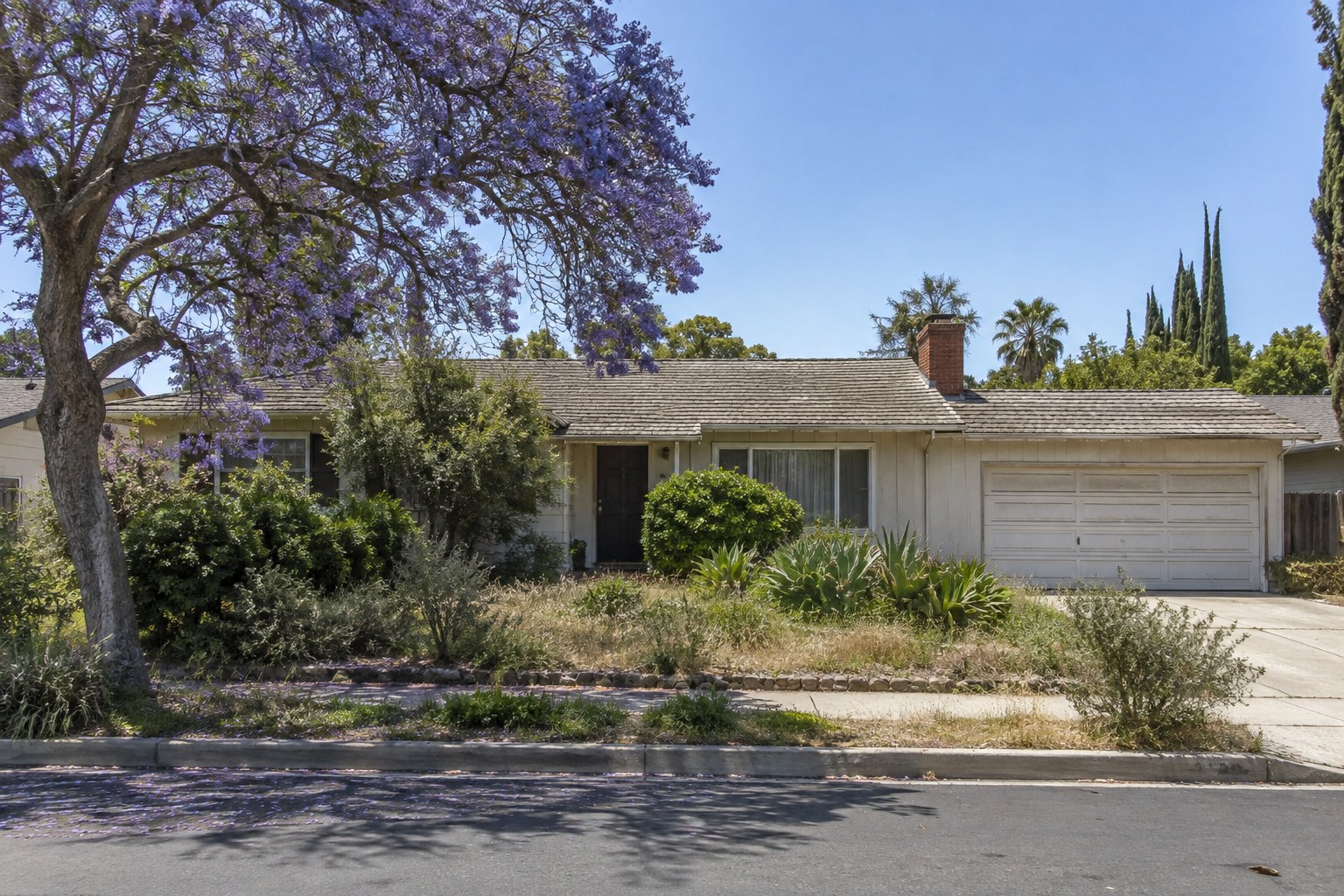 Dated 1960s single-story ranch house with an overgrown front yard in a Southern California neighborhood
