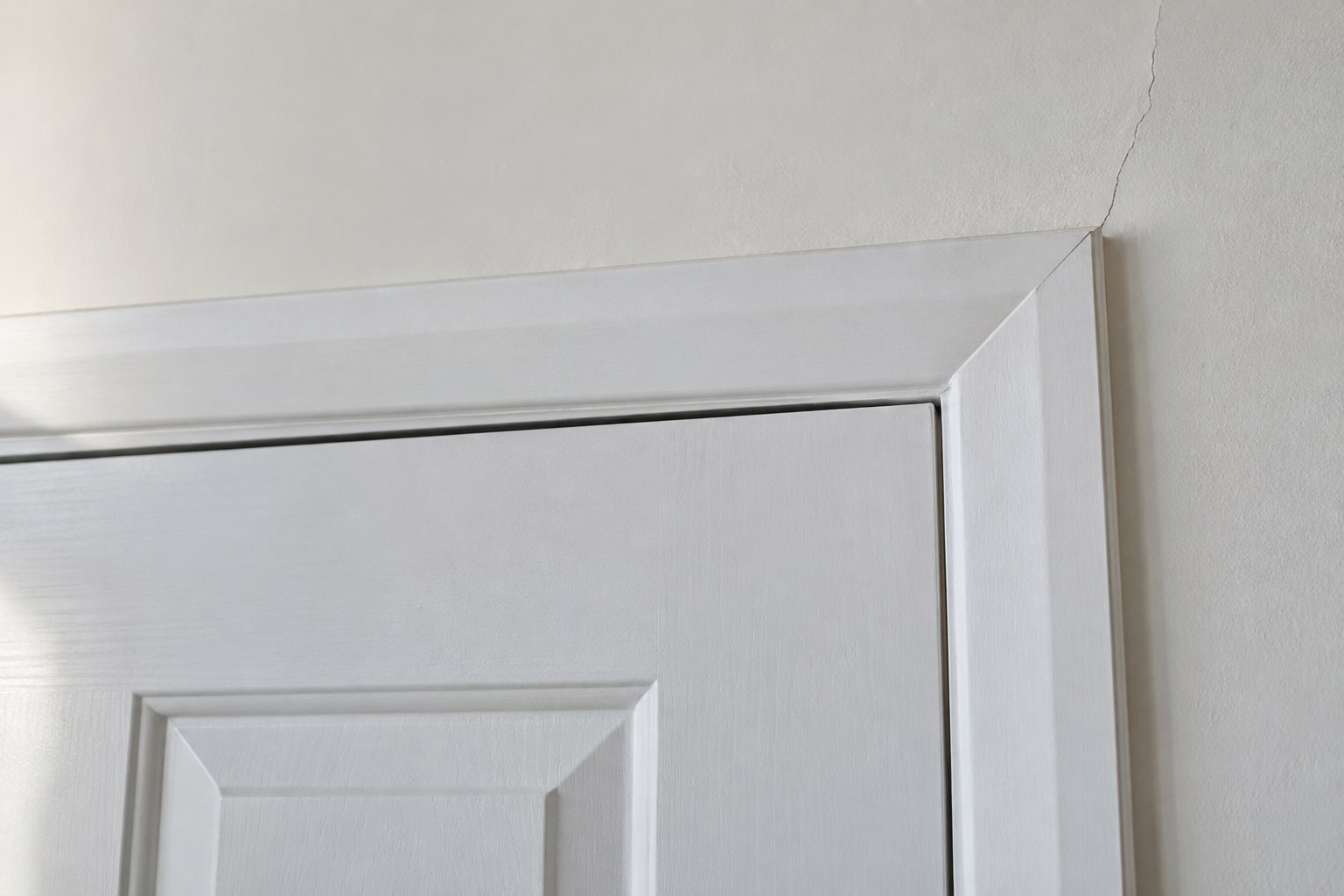 Tapered gap between the top of an interior door and its frame, with a hairline crack rising from the frame corner